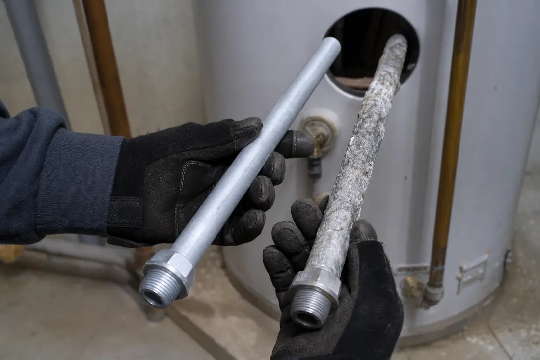 Mains gantées comparant une anode au magnésium usée et une anode neuve avant remplacement dans un boiler