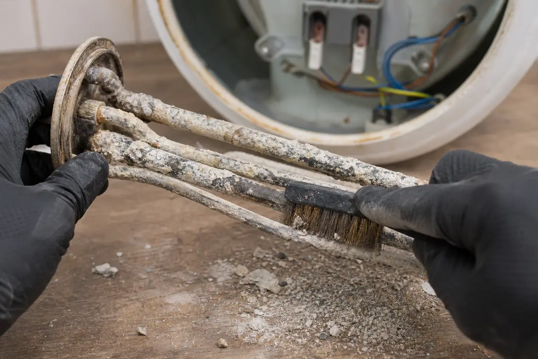 Mains gantées nettoyant le calcaire incrusté sur une résistance de chauffe-eau démontée